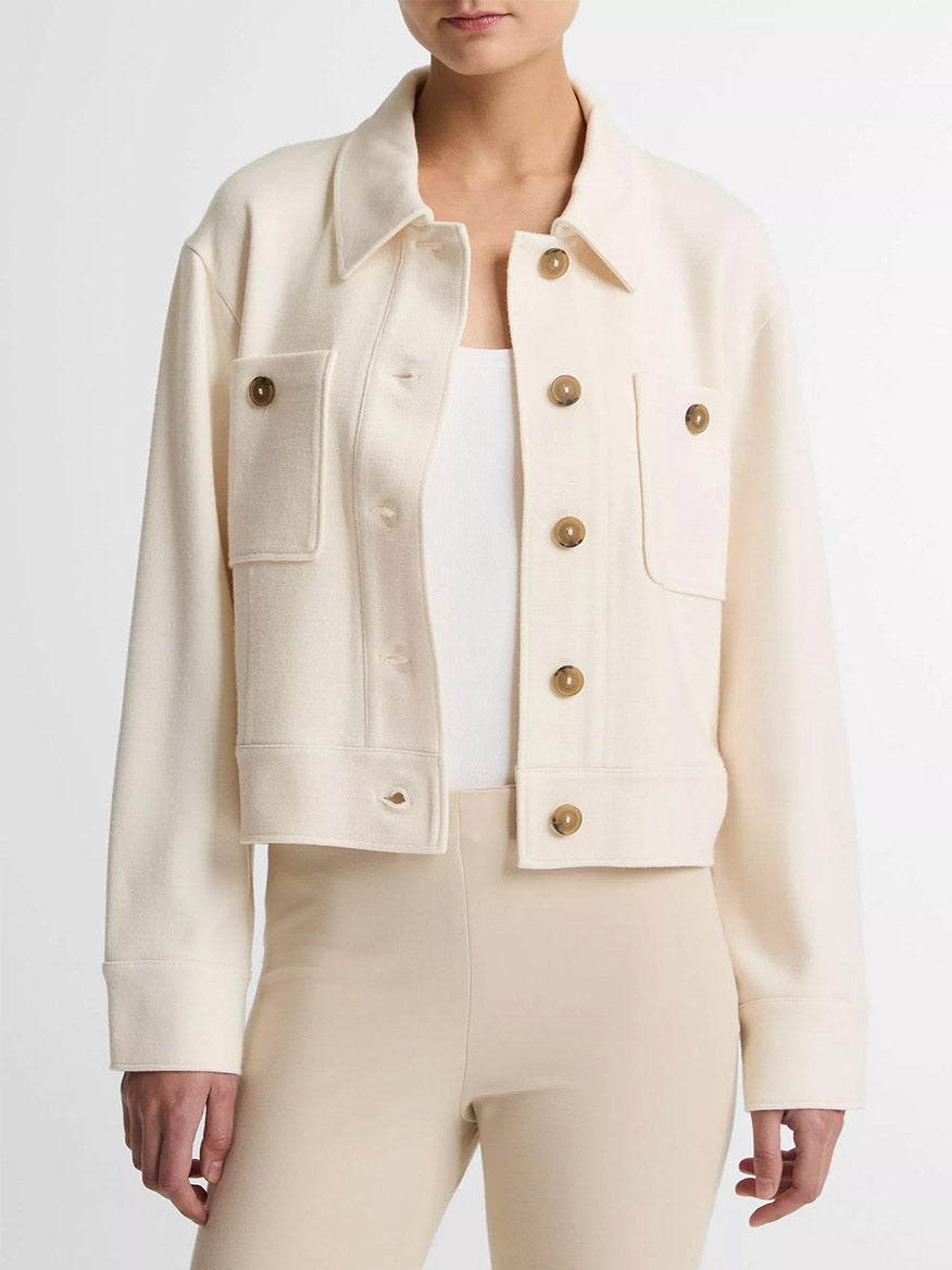 A woman wears the Vince Ponte Knit Jacket in Off-White, featuring chest pockets and a cropped silhouette, layered over a white top and beige pants, standing against a plain background.