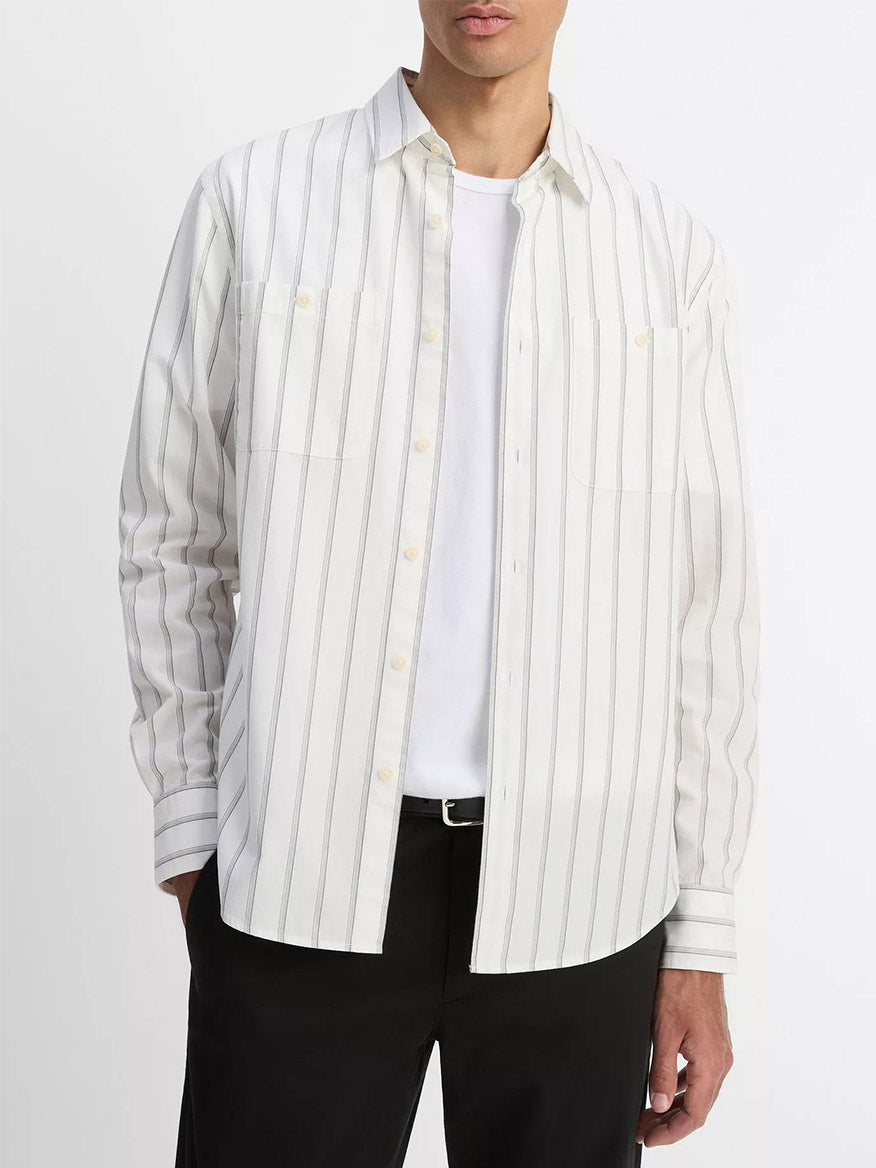 Wearing the Vince Port Stripe Cotton Button-Front Shirt in Off White/Smoke over a white t-shirt and black pants, this look offers an effortless, transitional staple against a plain backdrop.