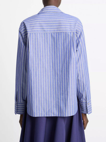 Person seen from the back wearing the Vince Striped Cotton Relaxed Popover Shirt in Pale Twilight—blue and white vertical stripes in breathable cotton poplin—paired with a dark blue skirt against a plain white background.