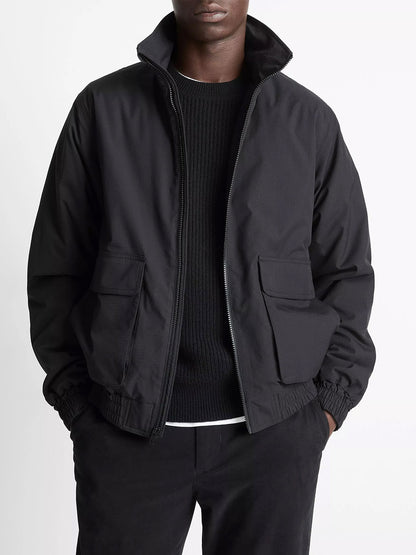 A person wears the Vince Italian Cotton Ripstop Bomber Jacket in Black, paired with a black sweater and black pants, standing hands-in-pockets against a plain background.