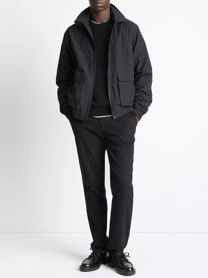 A person stands against a white background wearing the Vince Italian Cotton Ripstop Bomber Jacket in Black, paired with a black sweater, black pants, and black shoes, with hands in the jacket pockets.