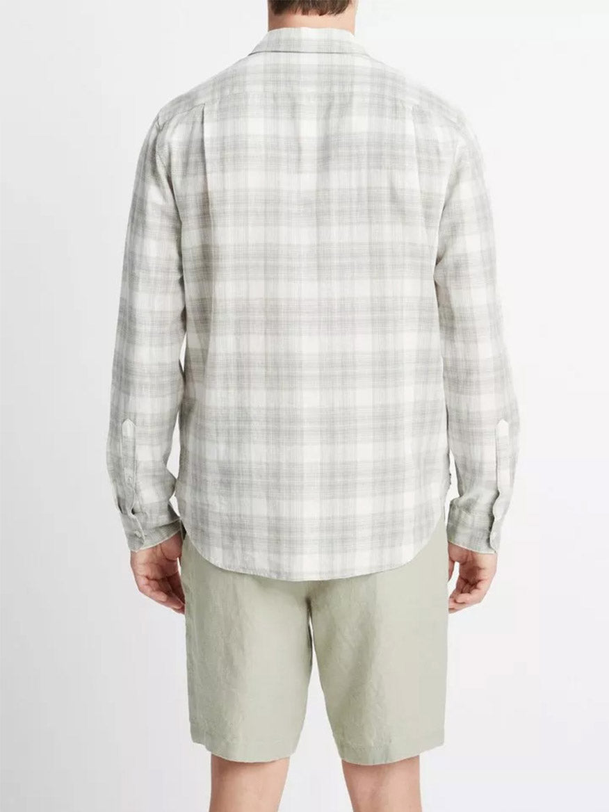 A man wearing a Vince Salton Plaid Long-Sleeve Shirt in Alabaster/Dried Cactus with linen-cotton construction and green shorts, viewed from the back, offering lightweight comfort.