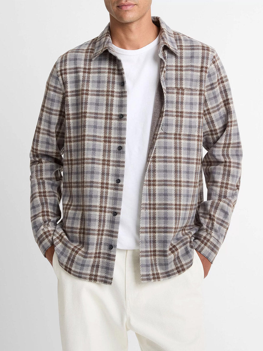 A man in a white tee and cream pants wears the Vince Plaid Cotton-Blend Shirt Jacket in Heather Fog Combo, featuring an ultra-soft gray, brown, and white plaid cotton-blend twill, standing with his hands in his pockets.
