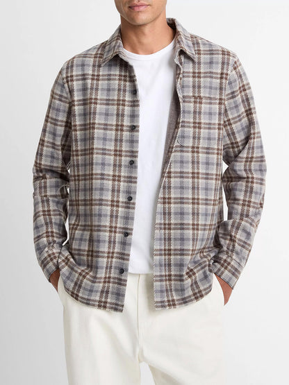 A man in a white tee and cream pants wears the Vince Plaid Cotton-Blend Shirt Jacket in Heather Fog Combo, featuring an ultra-soft gray, brown, and white plaid cotton-blend twill, standing with his hands in his pockets.