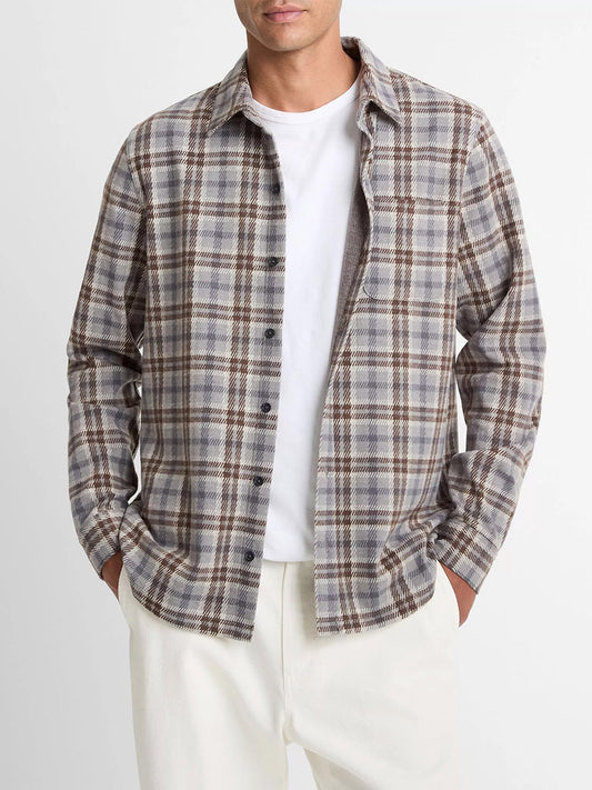 A man in a white tee and cream pants wears the Vince Plaid Cotton-Blend Shirt Jacket in Heather Fog Combo, featuring an ultra-soft gray, brown, and white plaid cotton-blend twill, standing with his hands in his pockets.
