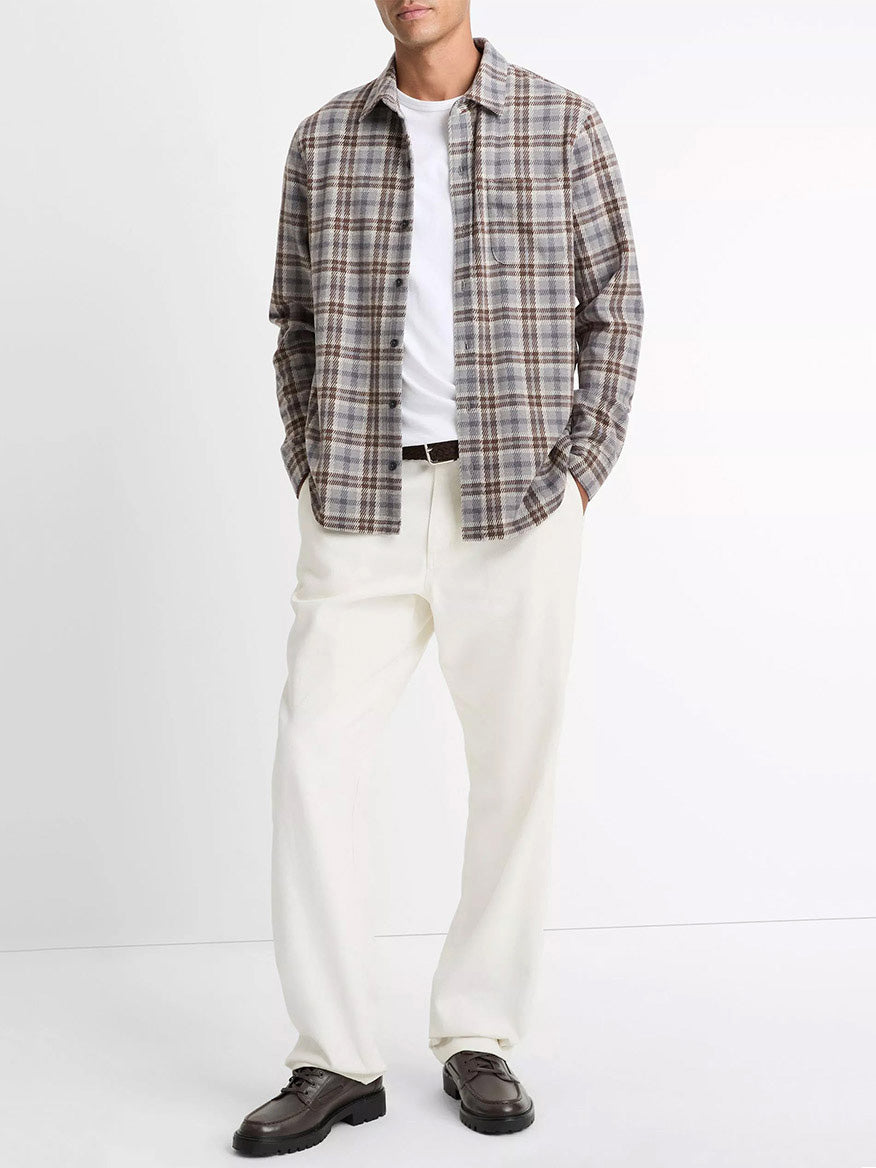 A man stands against a plain background wearing the Vince Plaid Cotton-Blend Shirt Jacket in Heather Fog Combo over a white t-shirt, paired with white pants and dark brown shoes.