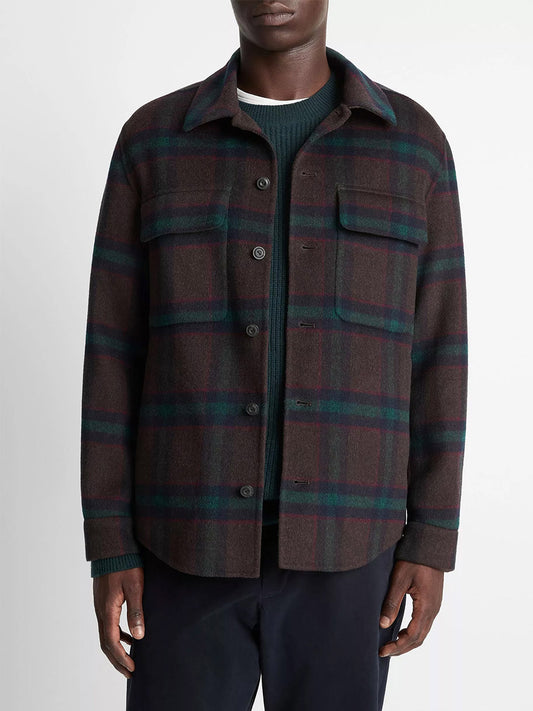 Wearing the Vince Plaid Splittable Wool-Blend Shirt Jacket in Coastal Country Racer, layered over a green sweater and dark pants, a person stands against a plain background.