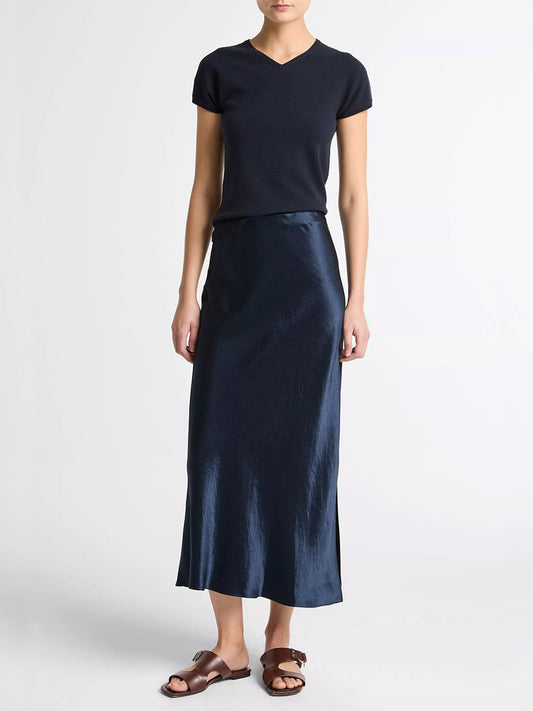 A person wearing a short-sleeve black top, the Vince Satin Side-Slit Slip Skirt in Coastal Blue, and brown sandals stands against a plain white background.