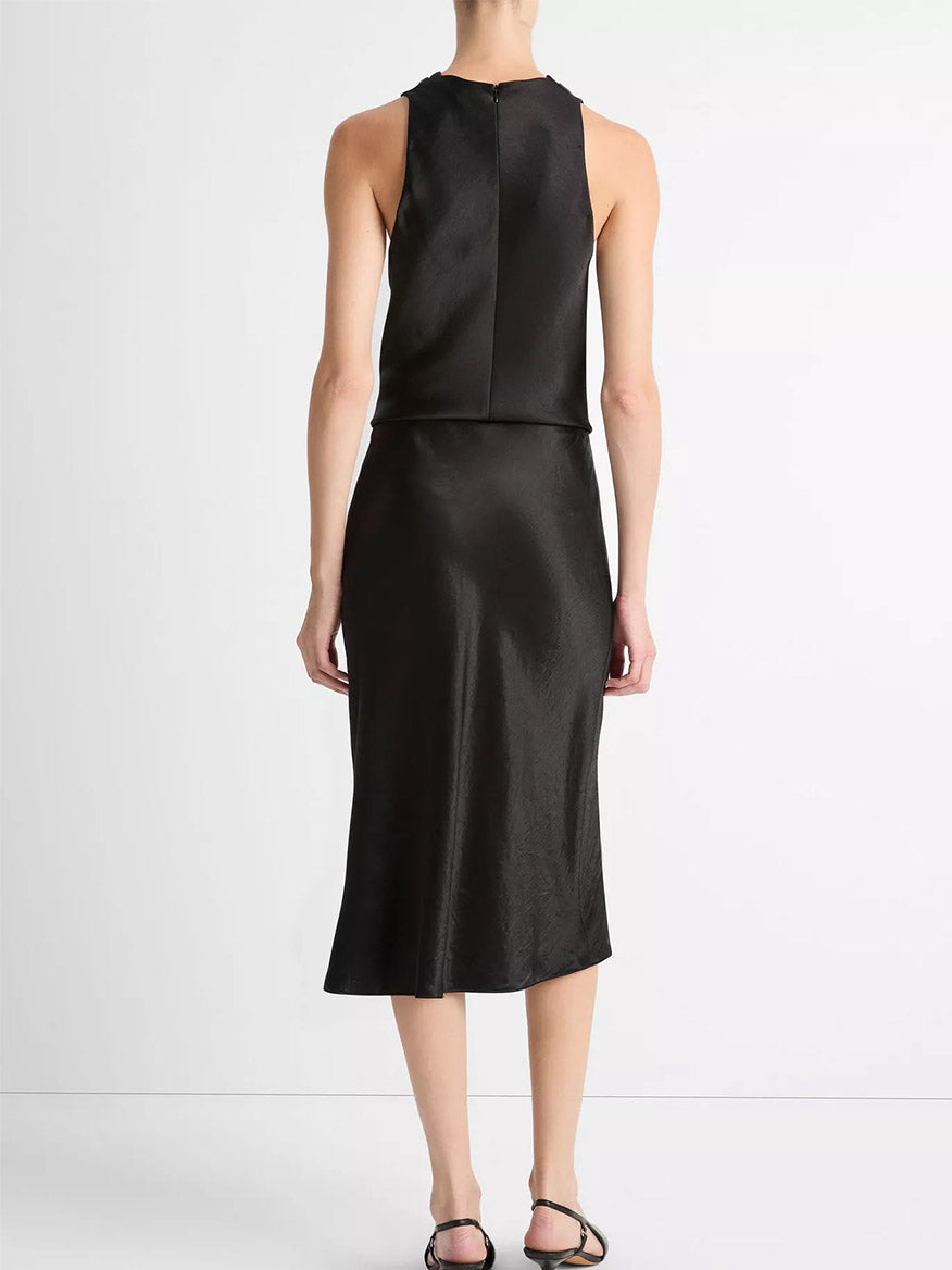 A person stands with their back to the camera against a plain white background, wearing the Vince Satin Slip Skirt in Black and black sandals.