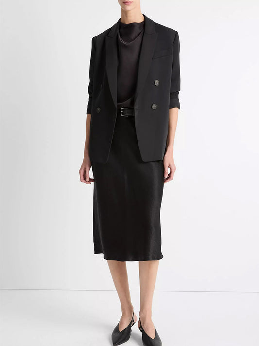 A person stands against a white background wearing a black double-breasted blazer, black top, pointed shoes, a black belt, and the Vince Satin Slip Skirt in Black.
