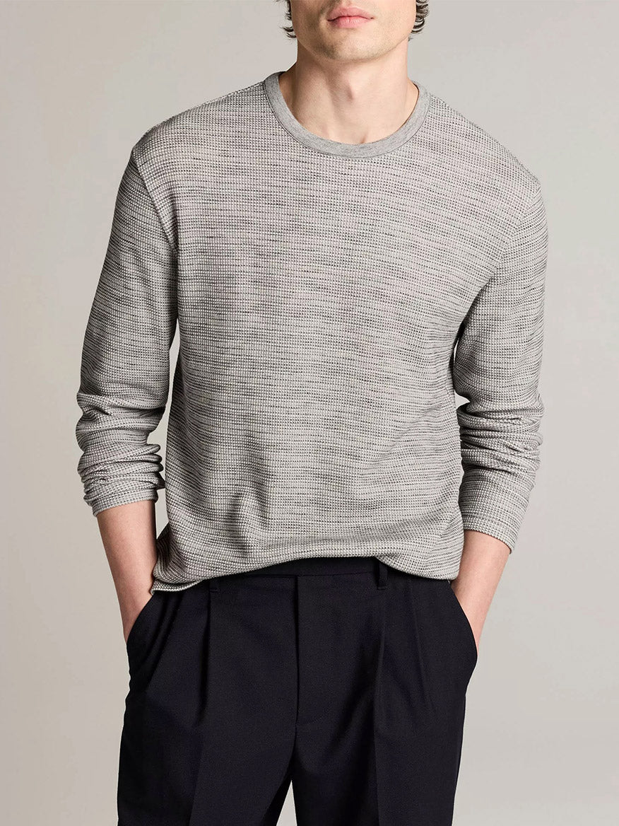 A man stands with his hands in his pockets against a neutral background, wearing the Vince Space-Dye Cotton-Blend Thermal Long-Sleeve T-Shirt in Late Evening Combo paired with black pleated trousers.