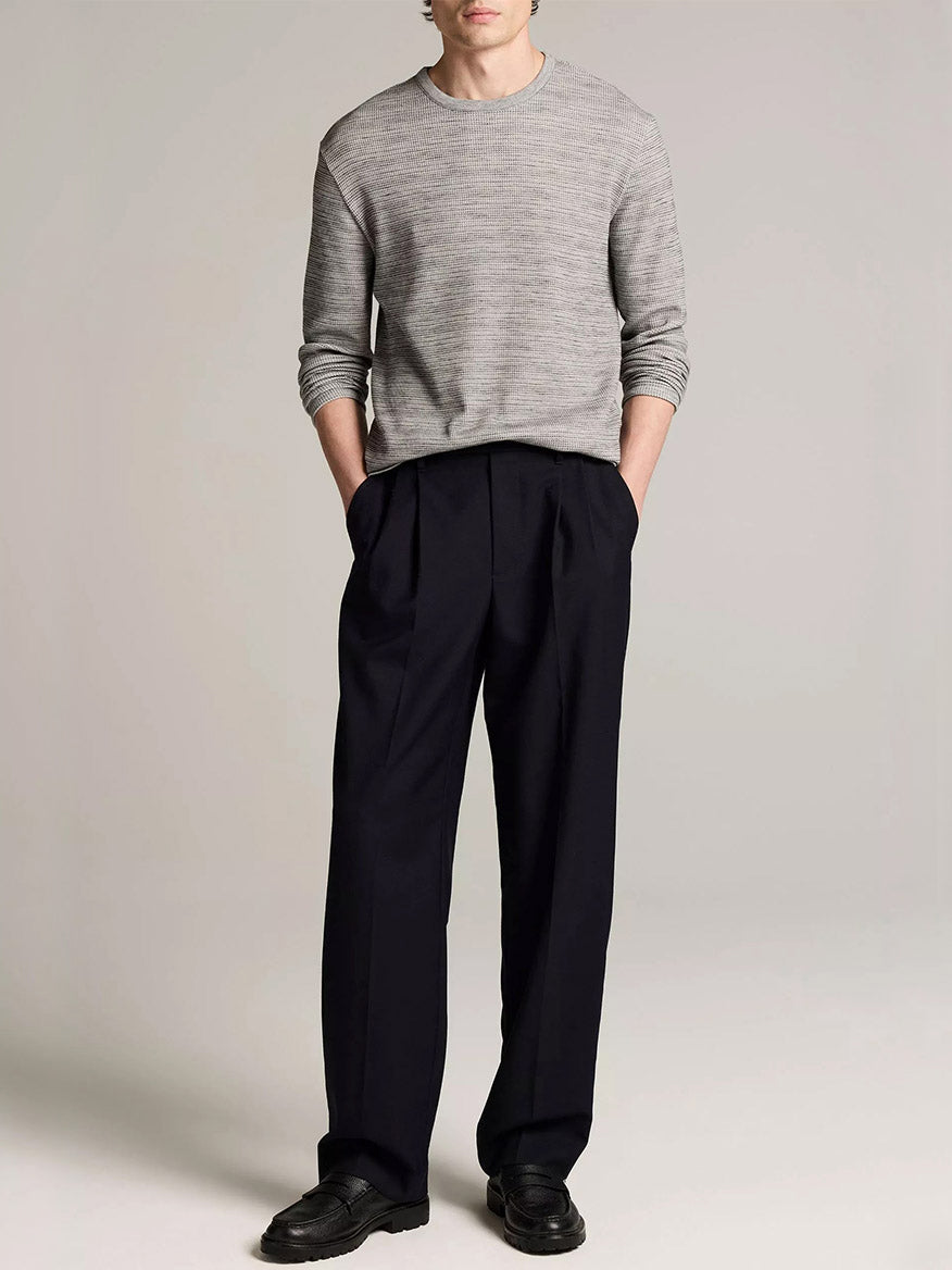 A person wearing the Vince Space-Dye Cotton-Blend Thermal Long-Sleeve T-Shirt in Late Evening Combo, paired with dark pleated trousers and black shoes, stands with hands in pockets against a plain background.