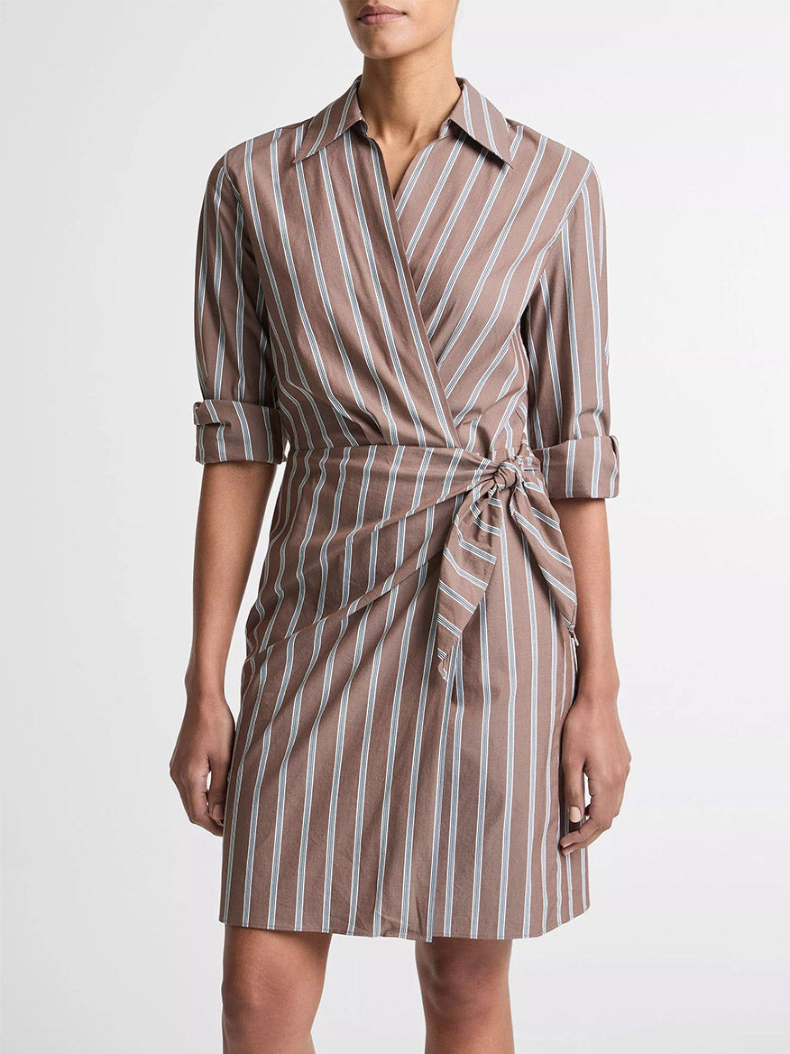 Woman wearing the Vince Striped Cotton-Blend Wrap Dress in Brown Multi, featuring a knee-length cut, white and blue vertical stripes, rolled long sleeves, and a waist tie for a flattering wrap silhouette.