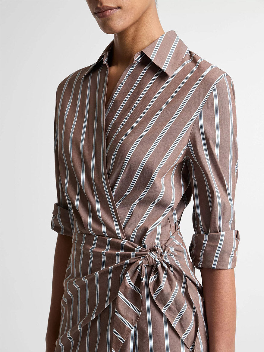 A person wearing the Vince Striped Cotton-Blend Wrap Dress in Brown Multi, featuring a wrap silhouette and rolled-up sleeves, shown from shoulders to waist.