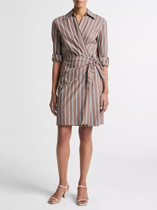 Someone wearing the Vince Striped Cotton-Blend Wrap Dress in Brown Multi, a knee-length, long-sleeve, collared wrap dress with vertical stripes and a side tie, styled with beige open-toe sandals.
