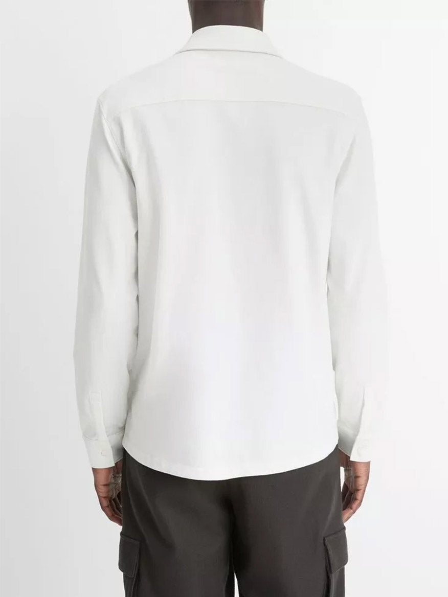 A person is standing with their back to the camera against a plain background, wearing an off-white Vince Sueded Cotton Jersey Button-Front Shirt, admired for its ultra-soft feel, along with dark cargo pants.