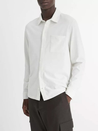 An individual dressed in the Vince Sueded Cotton Jersey Button-Front Shirt in off-white, featuring an ultra-soft texture, paired with dark pants against a plain backdrop.