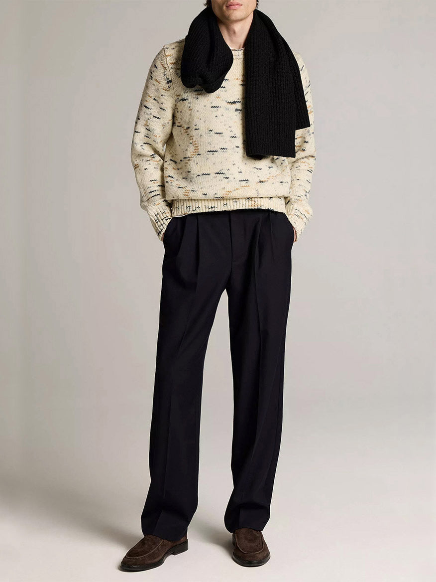 A person wears the Vince Super Space-Dye Merino Wool Sweater in Bone Combo, a black scarf, dark pleated trousers, and brown shoes against a plain background.