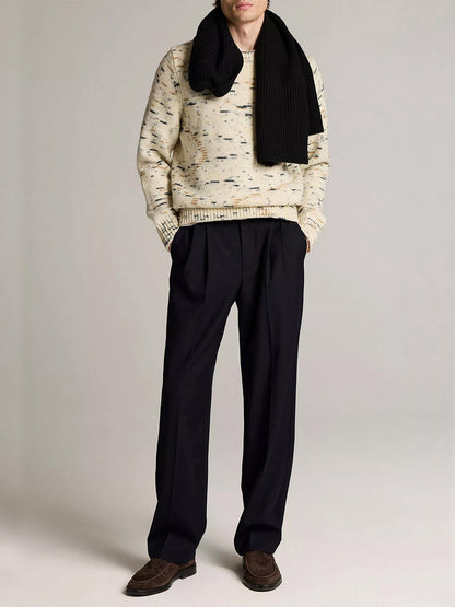 A person wears the Vince Super Space-Dye Merino Wool Sweater in Bone Combo, a black scarf, dark pleated trousers, and brown shoes against a plain background.