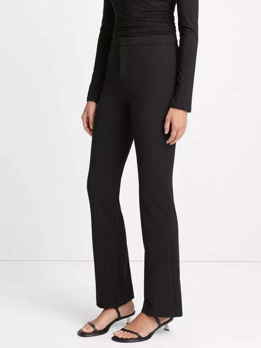 Woman clad in a black long-sleeve, slim fit top and Italian cotton, Vince Tapered-Leg Trouser in Black, paired with strappy sandals.