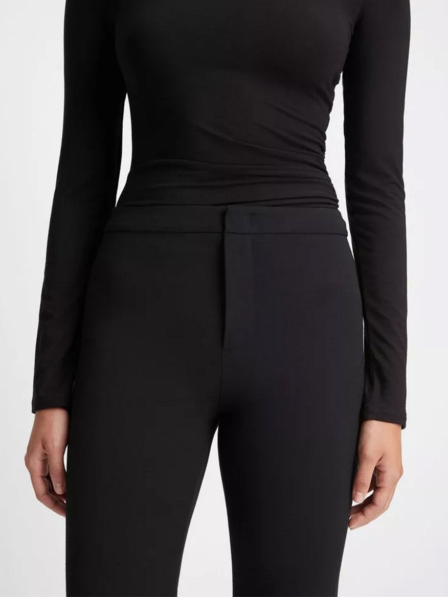 Close-up of a person wearing a black long-sleeve top and Vince Tapered-Leg Trouser in Black.