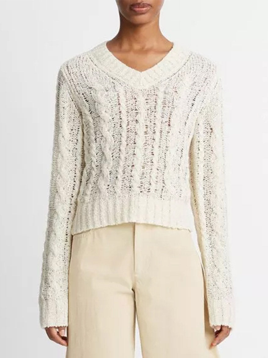 Woman wearing a Vince Textured Cable V-Neck Sweater in Cream with an open-knit design and beige pants.