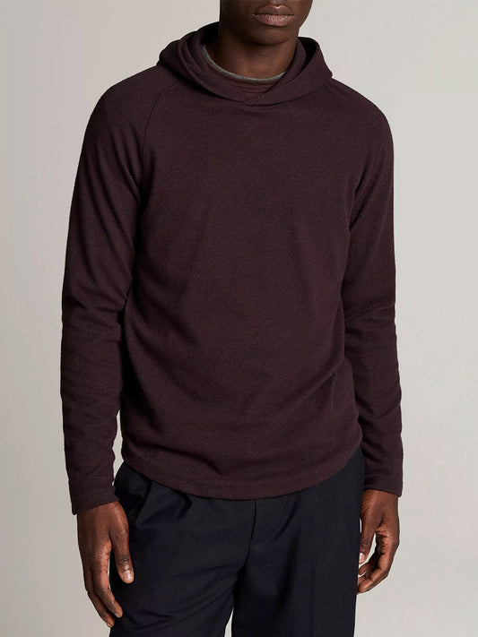 A person wearing the Vince Broken Twill Pullover Hoodie in Coastal Blue/Mahogany, crafted from a modal and cotton blend, paired with black pants, stands against a plain light background.