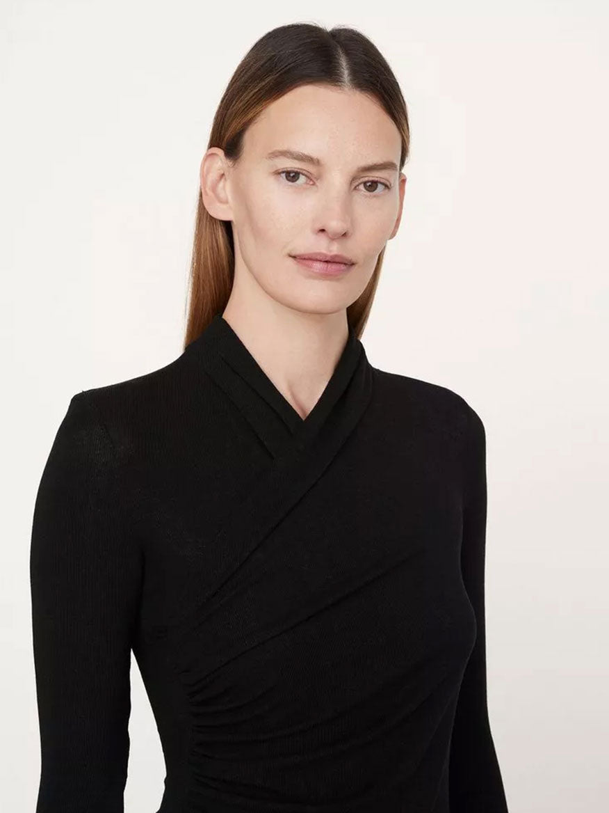 A woman with straight brown hair, wearing a Vince Fixed Wrap Long-Sleeve Top in Black that fits close to the skin, stands against a plain background, looking at the camera with a neutral expression.