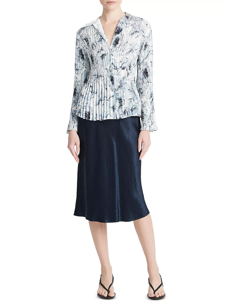 A person wearing a Vince Washed Lily Pleated Blouse in Pale Azure, navy skirt, and black sandals.