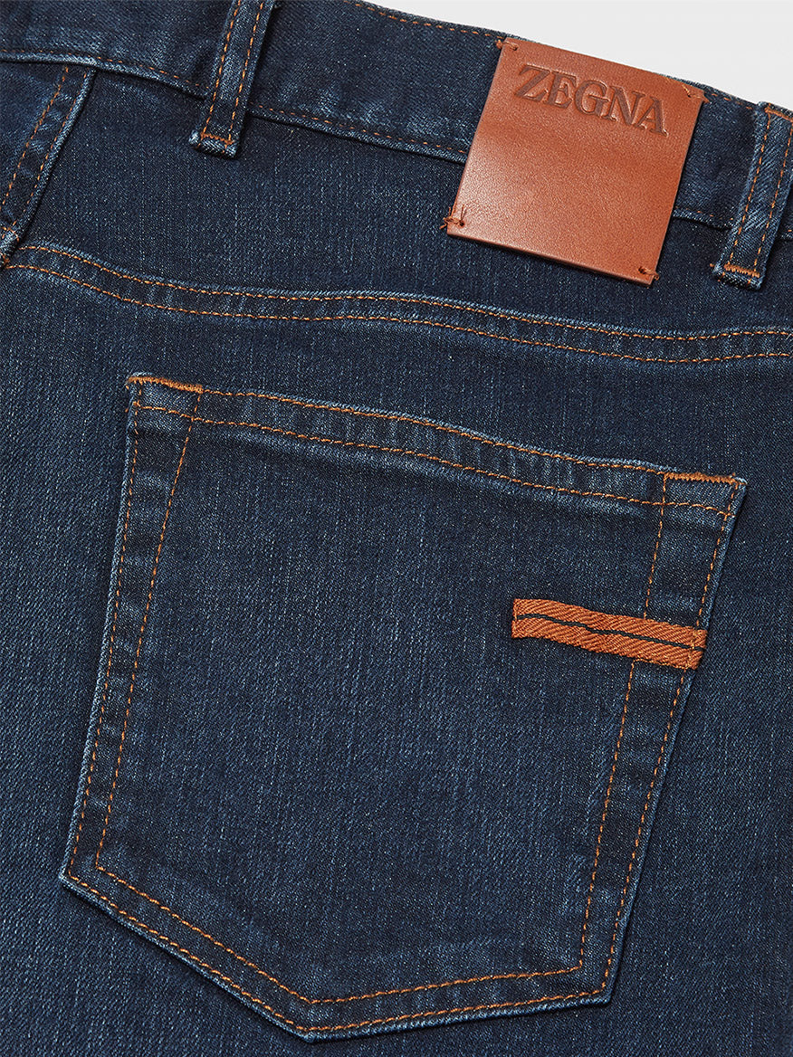 Close-up of the back pocket of regular fit blue jeans with orange contrast stitching and a leather patch label reading "ZEGNA" on the waistband, made from Zegna Classic Comfort Cotton Denim in Dark Blue.