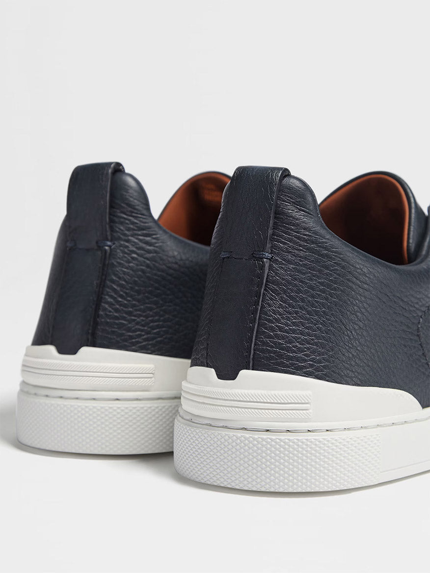 Close-up view of the back of two Zegna Navy Deerskin Triple Stitch™ sneakers with white rubber soles against a white background.