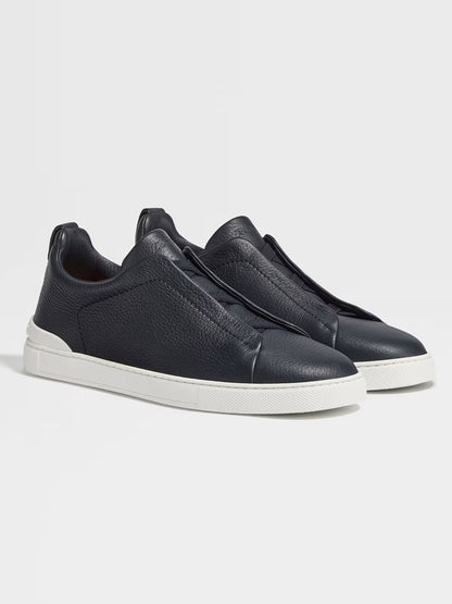 A pair of navy deerskin slip-on sneakers, similar in sleek design to the Zegna Navy Deerskin Triple Stitch™ Sneakers, featuring white rubber soles placed on a white background.