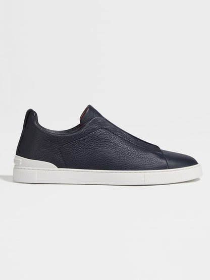 Navy deerskin slip-on sneaker with a white rubber sole shown in a side profile view, reminiscent of the sophisticated style of Zegna Navy Deerskin Triple Stitch™ Sneakers.