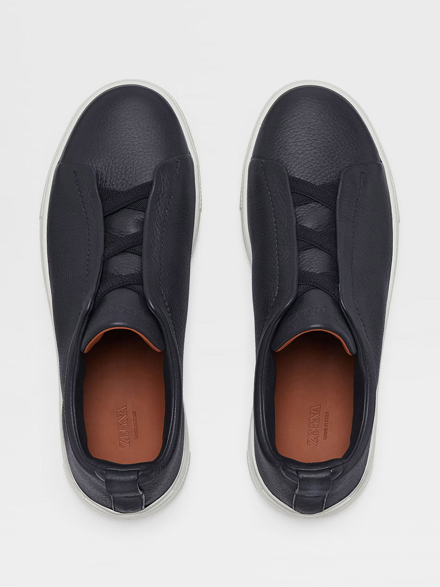 Top view of a pair of navy deerskin, Zegna Triple Stitch™ Sneakers with white soles, featuring a slip-on design with elastic bands across the top. The insoles are branded "Zegna".