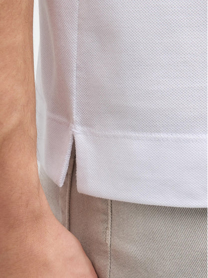 Close-up of a person wearing light-colored pants and a Zegna Polo Pure Cotton Piqué with Leather Trim Pocket in White with short sleeves and a side slit at the hem.