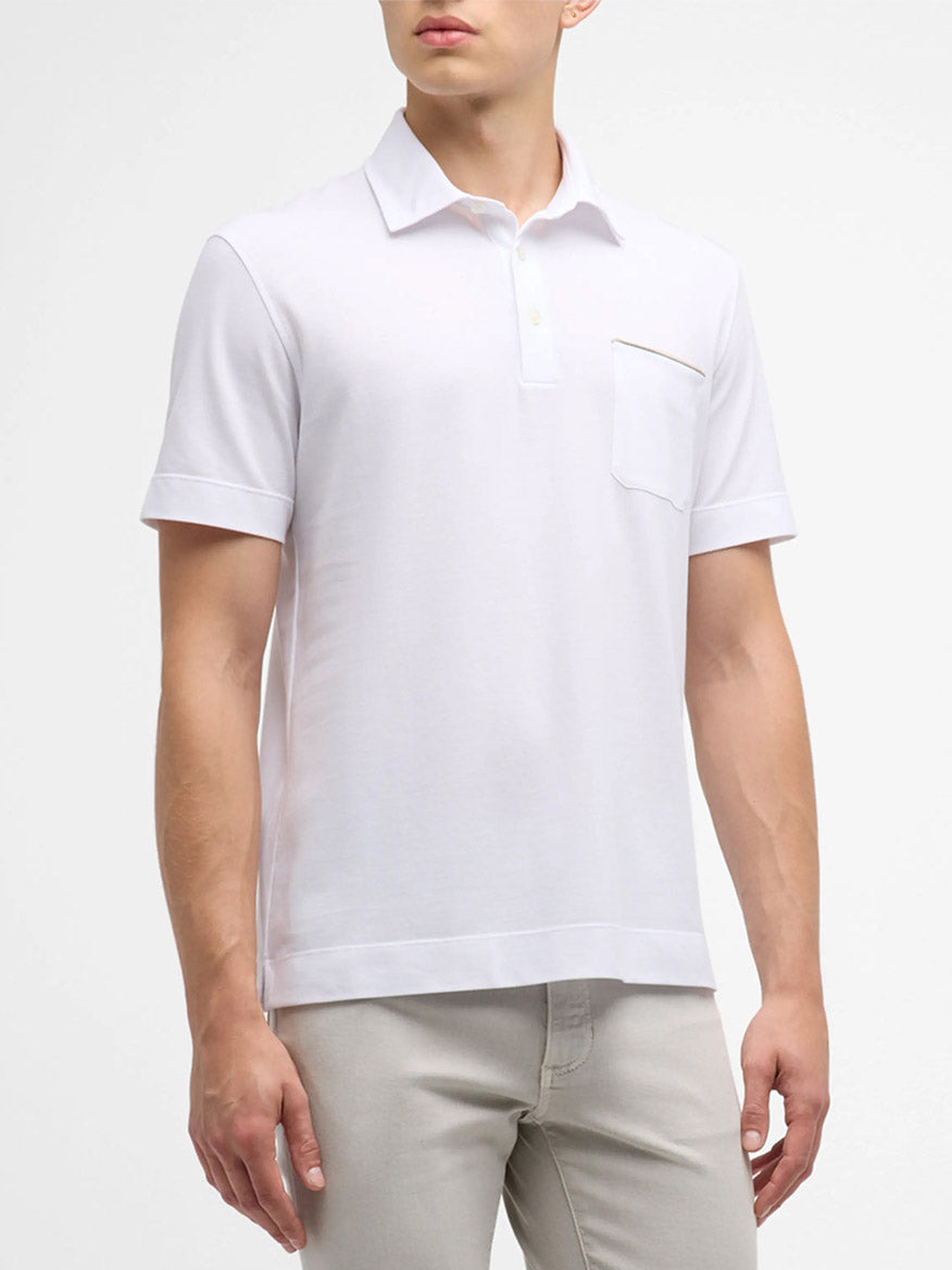 A person is wearing a Zegna Polo Pure Cotton Piqué with Leather Trim Pocket in White paired with beige pants. The shirt features a buttoned collar, and the background is plain white.