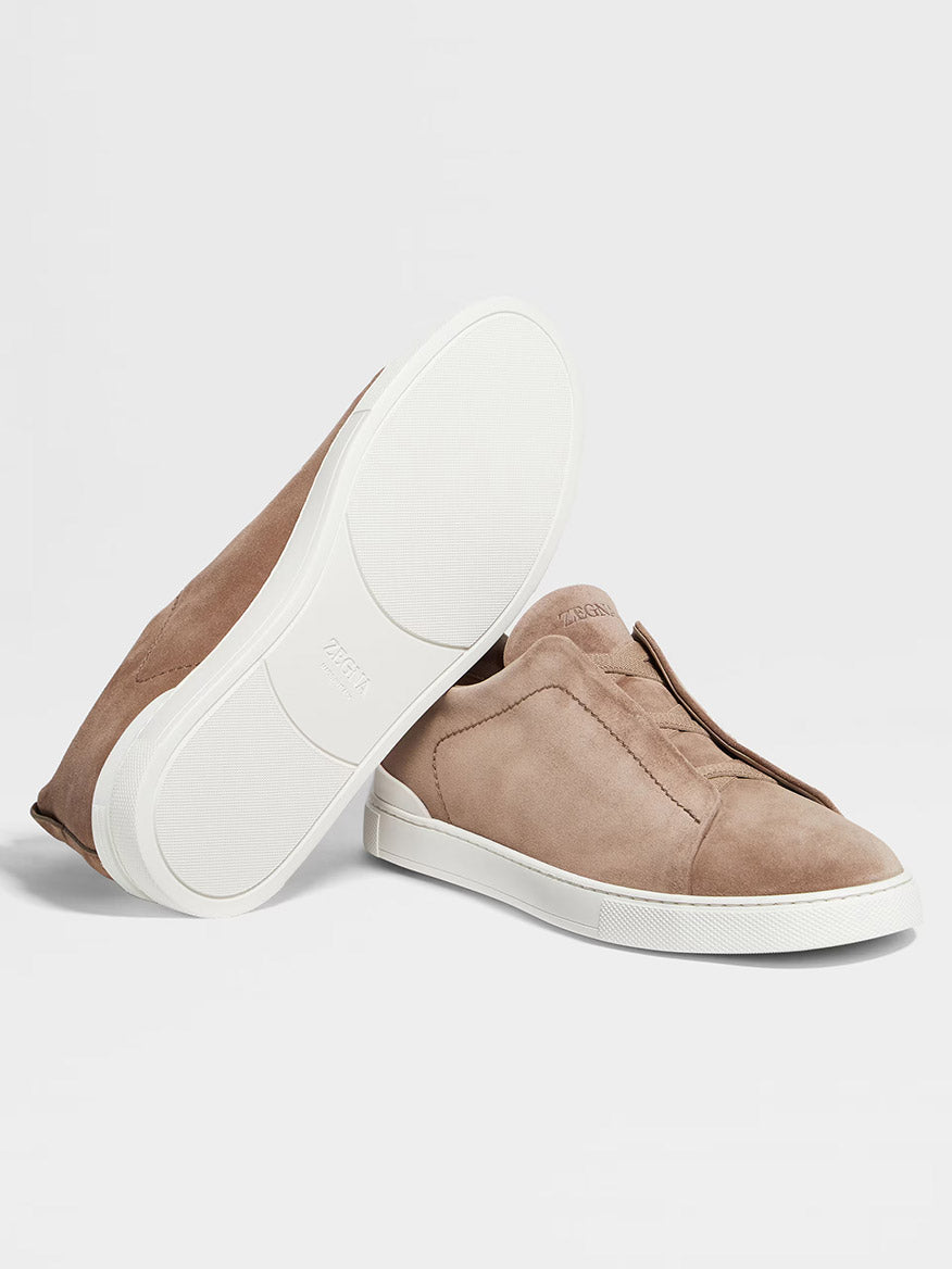 A pair of Zegna Beige Suede Triple Stitch Low Top Sneakers with white rubber soles, showcasing one shoe standing upright and the other lying on its side to display the sole.