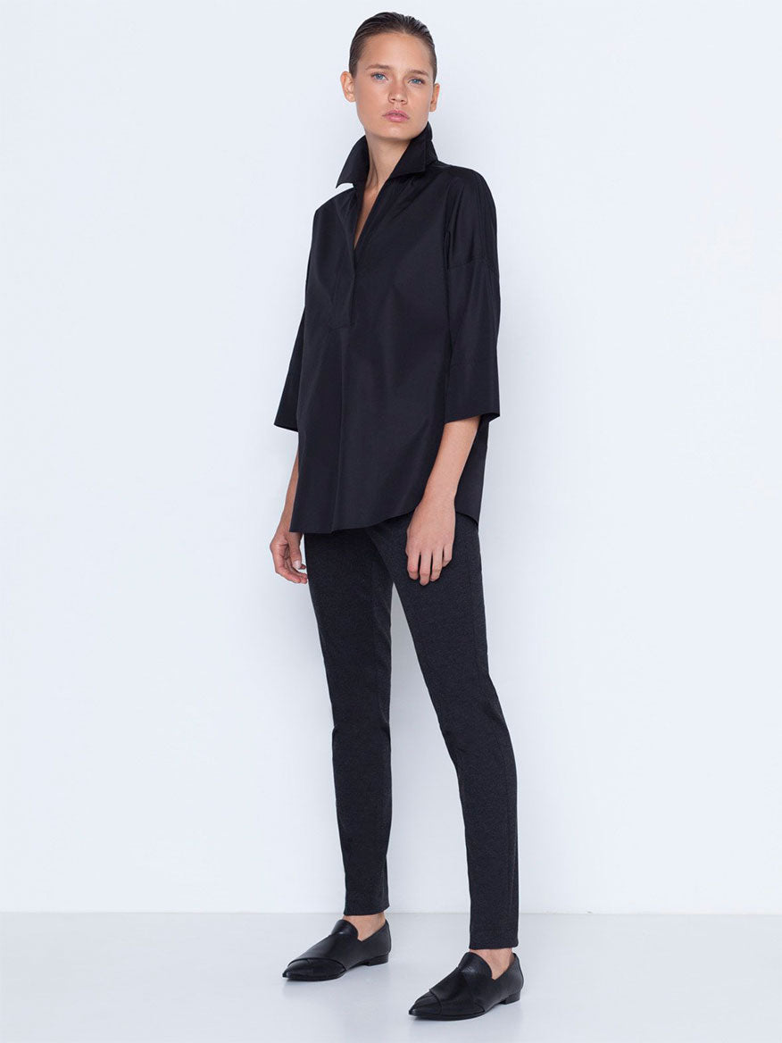 A woman in a black casual elegant outfit consisting of a blouse and the Akris Punto Mara Stretch Jersey Pants in Black with a front zip closure, paired with flat shoes, posing against a white background.