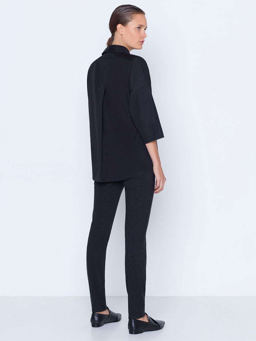 Sentence with product replaced: Woman standing sideways wearing a black tunic and Akris Punto Mara Stretch Jersey Pants in Black with black shoes, featuring a front zip closure.