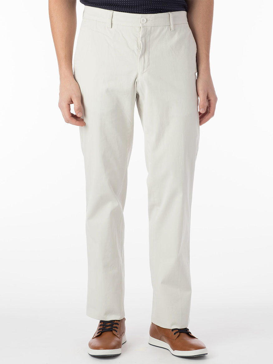 A person wearing the Ballin Atwater True Khaki Modern Flat Front Pant in Stone and brown lace-up shoes stands against a plain white background. The pants, made of lightweight Pima cotton, are secured with a button and zipper.