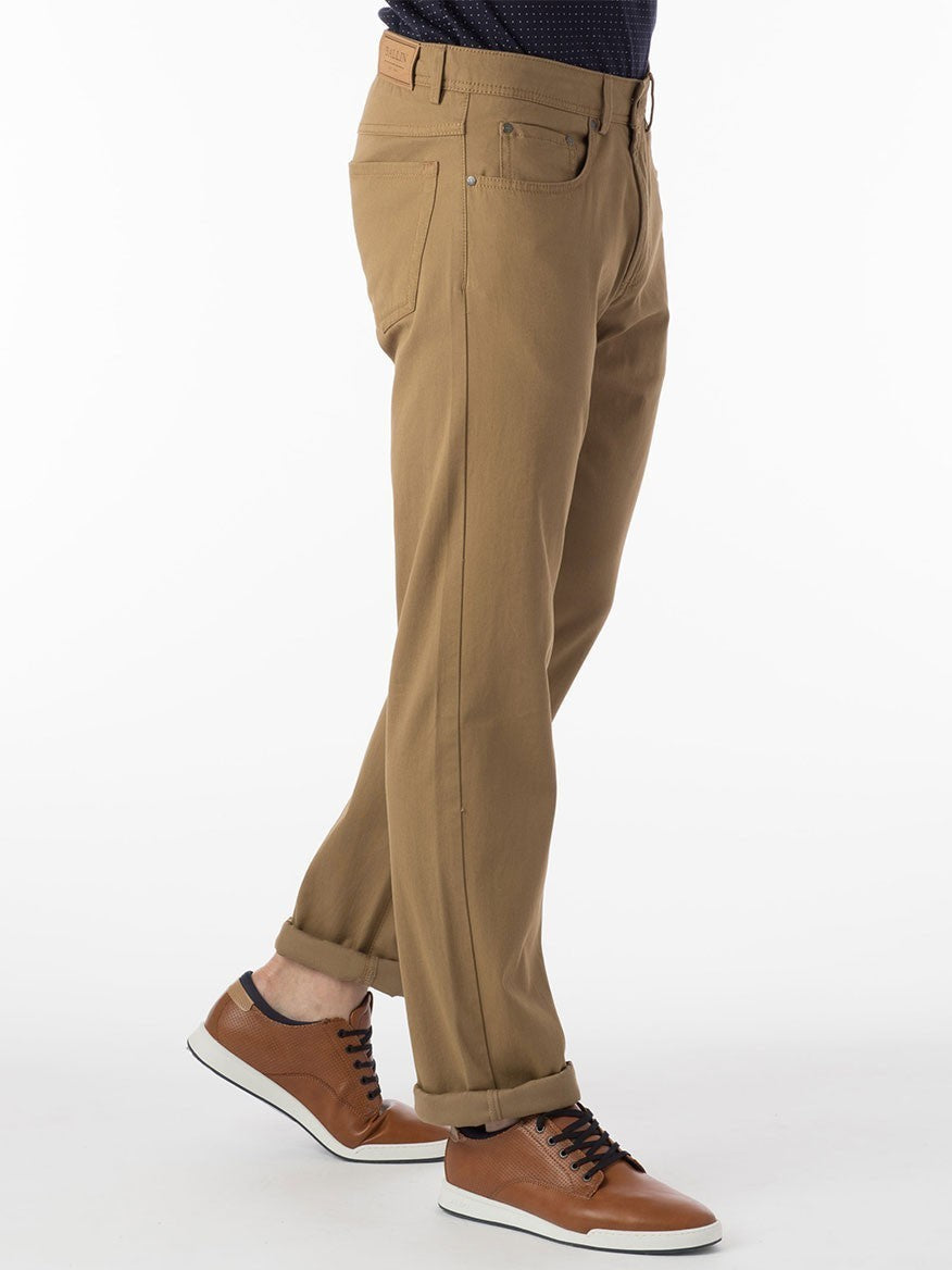A man donning Ballin Crescent Modern 5 Pocket Twill Pants in British Tan and a black shirt exudes exceptional comfort and embodies a business casual style.