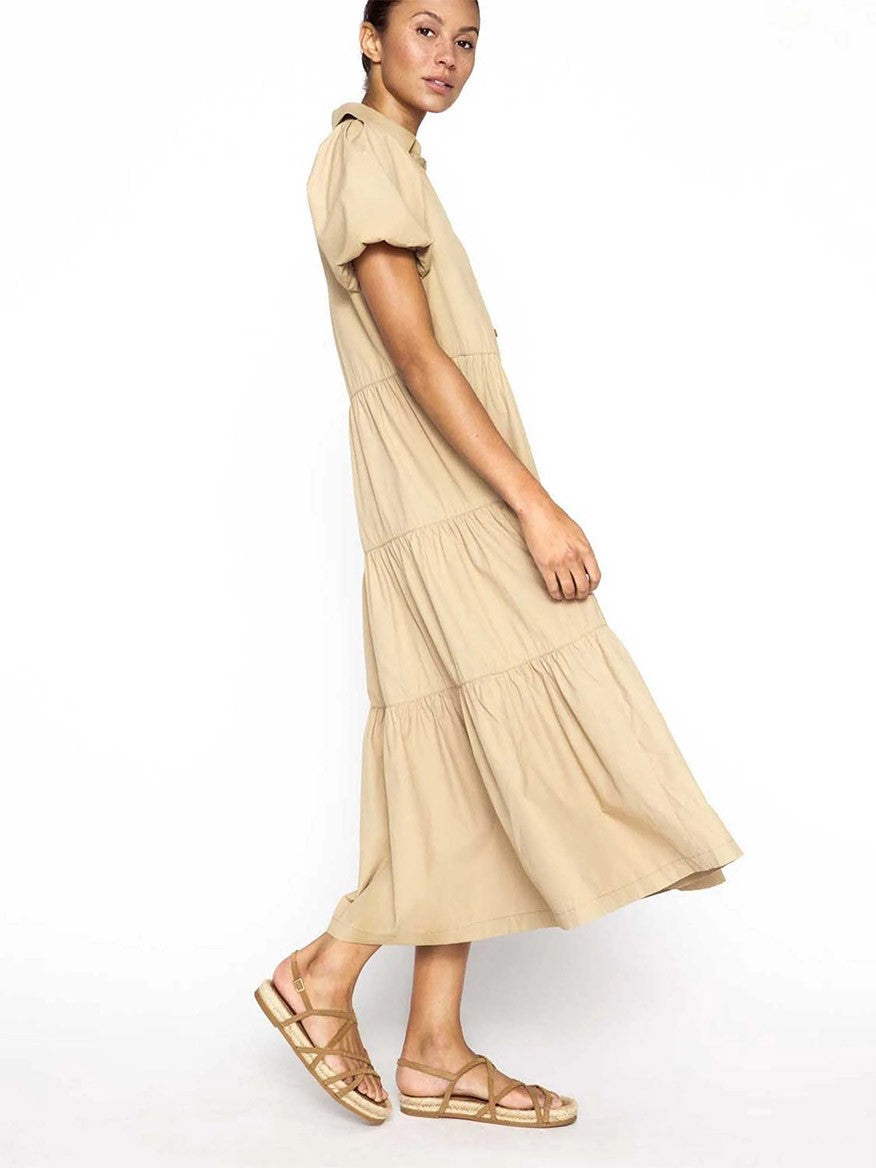 A woman poses in a Brochu Walker Havana Dress in Sahara with short sleeves and a tiered skirt, showcasing feminine appeal, paired with strappy sandals.