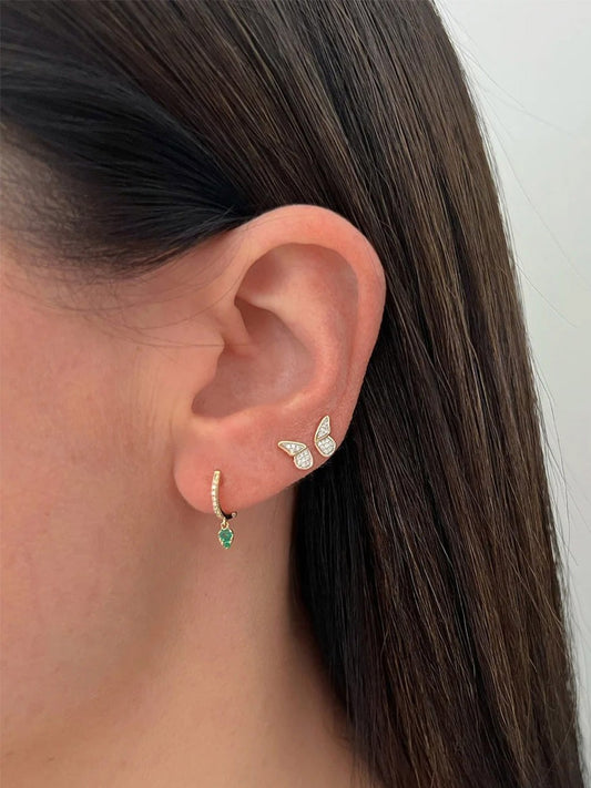 A person with dark hair wearing EF Collection Diamond Flutter Stud Earrings in Yellow Gold, featuring a gold earring with a green gemstone and a diamond butterfly-shaped stud in the upper ear.