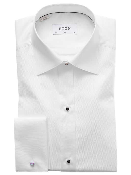 A folded white dress shirt with black buttons, a spread collar, and a tag labeled "Eton Slim Fit Piqué Black Tie Dress Shirt," made from premium piqué fabric.