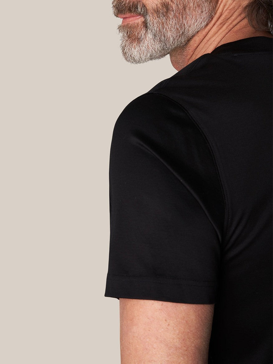 Profile view of a man with a beard wearing an Eton Filo di Scozia T-Shirt in Black against a beige background.