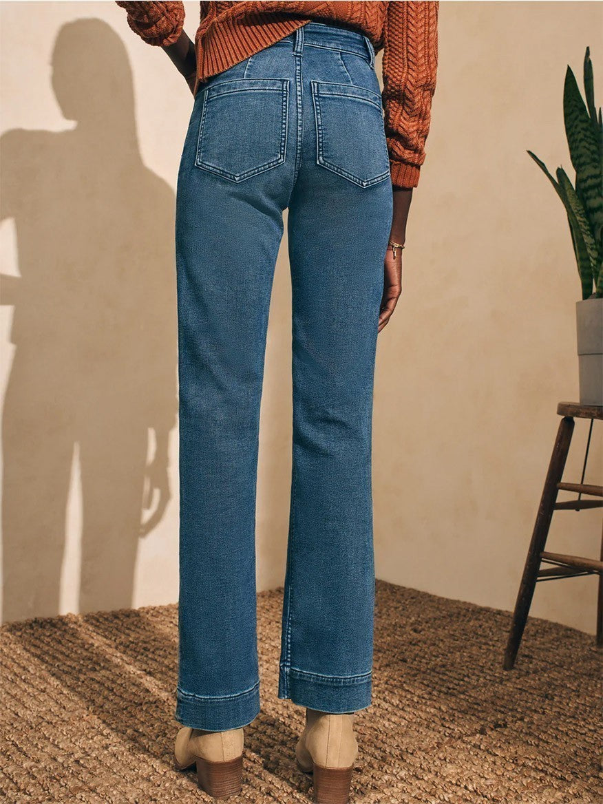 A person wearing Faherty Brand Stretch Terry Slim Wide Leg Pant in Riverton Wash and beige boots stands with their back to the camera, in a room casting a shadow on the wall. The pants are in a relaxed fit style.