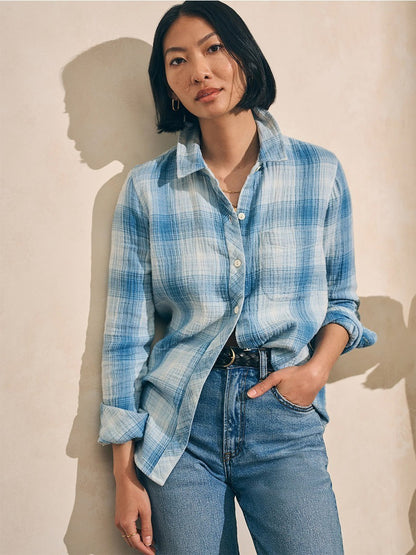 A woman wearing the Faherty Brand Malibu Shirt in Indigo Plaid, a relaxed fit button-up shirt made of double cloth fabric, standing against a wall.
