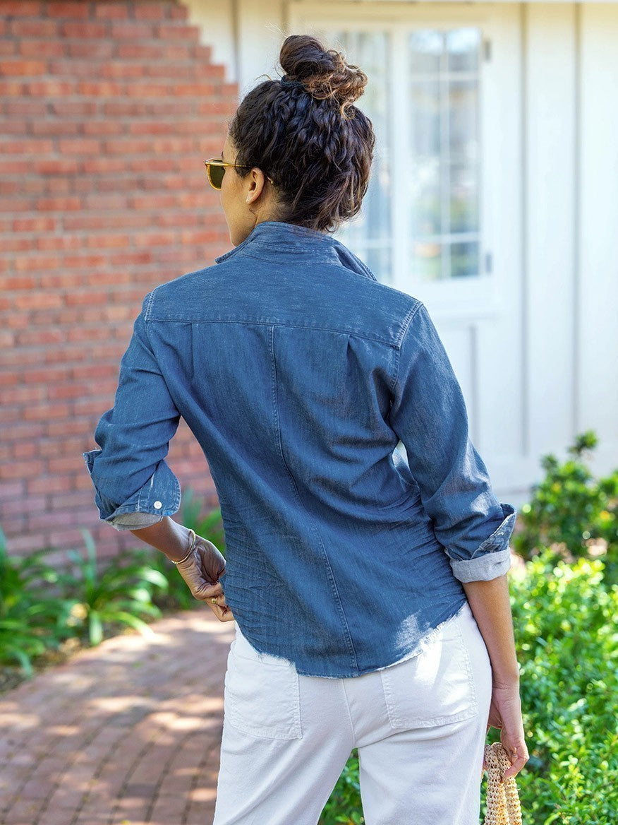 Barry, a woman wearing white pants and a denim shirt, dons a Frank & Eileen Barry Tailored Button-Up Shirt in Vintage Indigo.