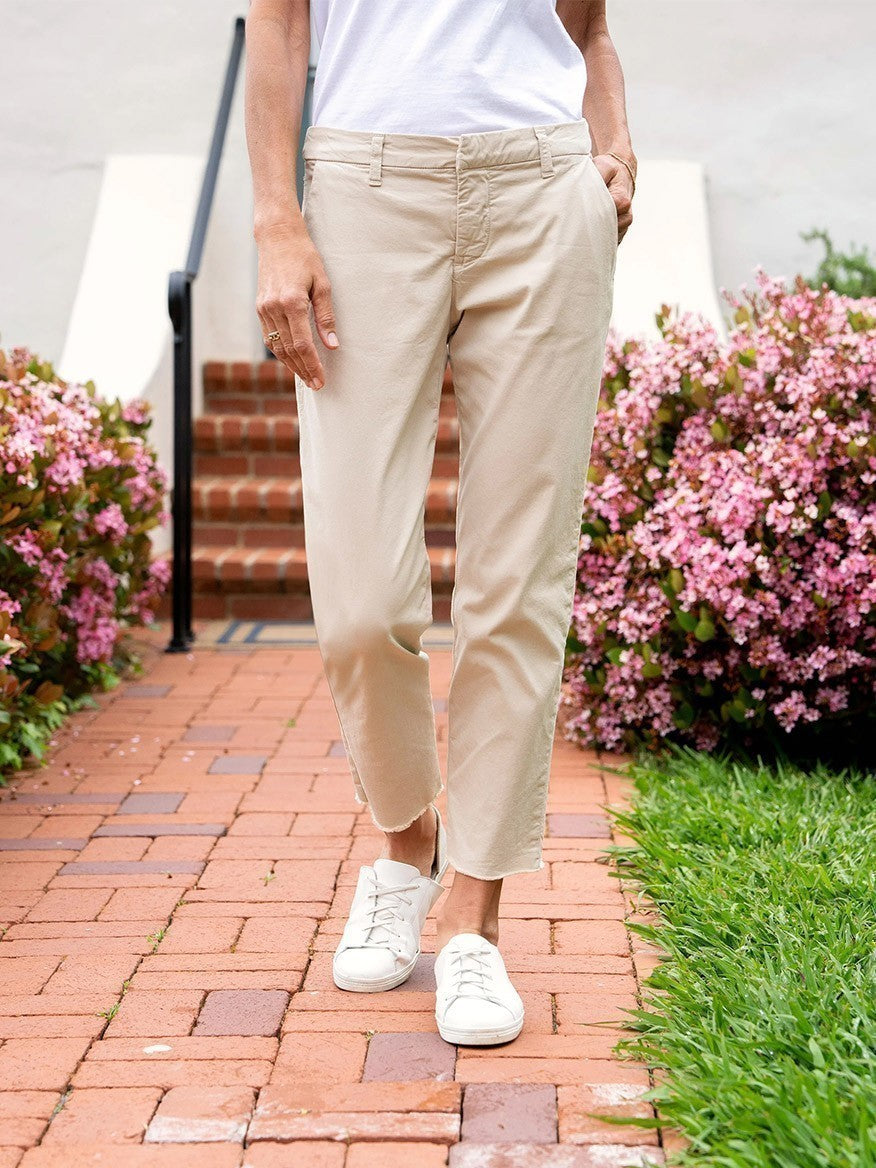 A person wearing Frank & Eileen Wicklow Italian Chino in Khaki with a relaxed fit and white sneakers standing on a brick pathway with flowers in the background.