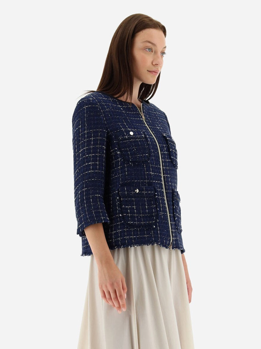 A woman exudes elegance in a New Blue Herno Jacket in Casual Tweed with front pockets and a white skirt, set against a crisp white background. The jacket's fabric catches the light, subtly hinting at the allure of understated luxury.